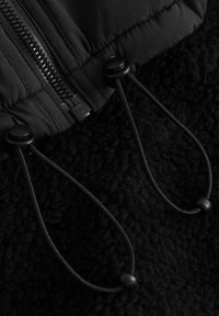 Giacca nera con zip, dotata di una morbida fodera interna texturizzata. Presenta lacci neri con toggles e una zip YKK. Vista ravvicinata.