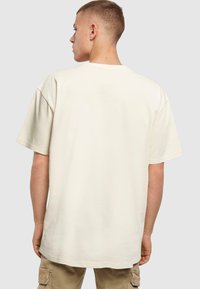 Lys beige t-skjorte laget av bomull, med rund hals og korte ermer. Bakdelen har en avslappet fit uten bemerkelsesverdige mønstre.