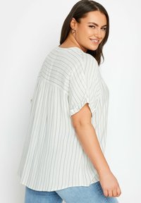 Blusa leggera a righe in verde chiaro e bianco, caratterizzata da una vestibilità informale, maniche arrotolate e dettagli arricciati sul retro.