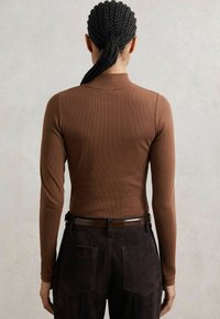Maglietta a maniche lunghe marrone a coste dal design aderente, abbinata a pantaloni scuri in suede marrone con tasche a marsupio e una cintura liscia.