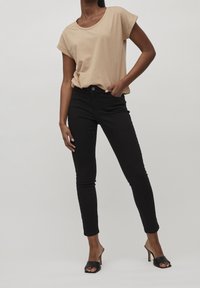 Beige tričko s krátkým rukávem v kombinaci s černými slim kalhotami a černými sandály na podpatku s otevřenou špičkou. Hladký materiál, neformální design, přiléhavý střih.