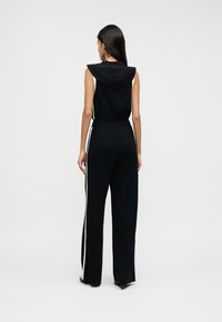 Μαύρη ολόσωμη φόρμα χωρίς μανίκια με κουκούλα, με πλαινές ρίγες και άνετη εφαρμογή. Ομαλή υφή με ελαφρώς στενή γραμμή στο πόδι.