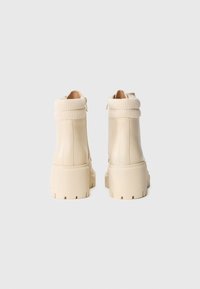 Bottines en cuir beige avec col en maille côtelée, semelle épaisse et zip latéral ; texture lisse avec semelle crantée pour une meilleure adhérence.