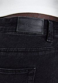 Černé denimové džíny s viditelnou koženou etiketou s nápisem "ONLY CARMAKOMA", s texturovaným povrchem a jemnými švy.