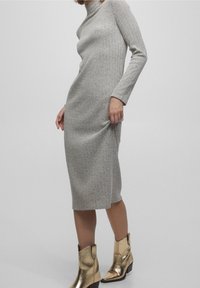 Robe en tricot gris à manches longues et col haut, avec une texture côtelée, associée à des bottines dorées métalliques.