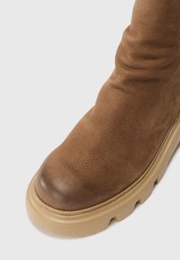 Brune lær ankle boot med en rund tå, teksturert overdel og tykk beige såle. Har et lett slappet design og minimal søm.