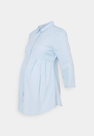 Blouse de maternité bleu clair à manches longues, avec ouverture boutonnée sur le devant, taille plissée et col, présentée sur fond blanc.