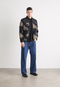 Fleece jakk mustade kunstnahast aktsentidega, millel on sinine ja beež abstraktne muster. Kombineeritud lõdva lõikega siniste teksade ja mustade kingadega.