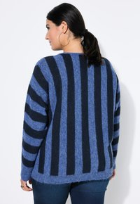 Niebieski sweter w paski w odcieniach granatu o miękkiej teksturze, z długimi rękawami i lekko oversize’owym krojem. Tył posiada pionowe paski oraz zaokrąglony dół.