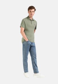 Polo verde con cuello y mangas cortas, combinado con jeans de color azul claro y zapatillas blancas. Cuenta con un logotipo en el pecho.