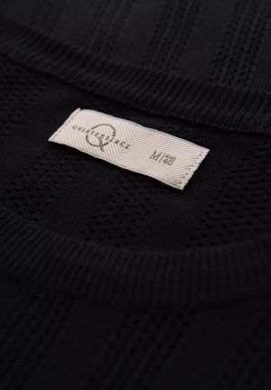 Sort striktrøje med et struktureret vævet mønster og en ribbet krave. Undersiden viser et mærkat med brand- og størrelsesoplysninger.