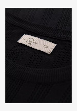 Sort striktrøje med et struktureret vævet mønster og en ribbet krave. Undersiden viser et mærkat med brand- og størrelsesoplysninger.