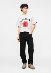 Λευκό t-shirt με κοντά μανίκια, με γράφημα "ICECREAM" και κόκκινο ηλιοειδές σχέδιο, συνδυασμένο με μαύρο τζιν και ανοιχτό γκρι σουέτ μποτάκια.