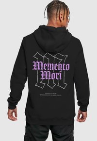 Svart hettegenser med teksten "Memento Mori" i lilla gotisk skrift. Bakdesignet har tilleggstekst med hvit omriss.