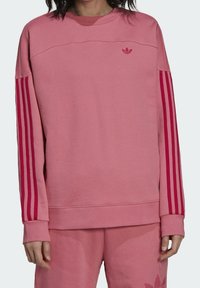 Rosa sweatshirt av mjukt tyg, med rund halsringning, långa ärmar och röda vertikala ränder på ärmarna. Liten logotyp på bröstet.