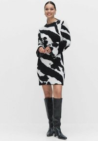 Neulemekko musta-valkoisella lehmäkuviolla, jossa on pitkät hihat ja rento istuvuus. Yhdistetty polvenkorkuisiin mustiin nahkabootseihin.