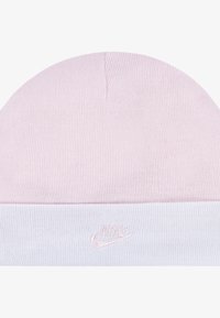 Roza pletena kapa s bijelim rubom, koja ima vezeni Nike logo. Glatka površina, mekani materijal i zaobljen oblik.