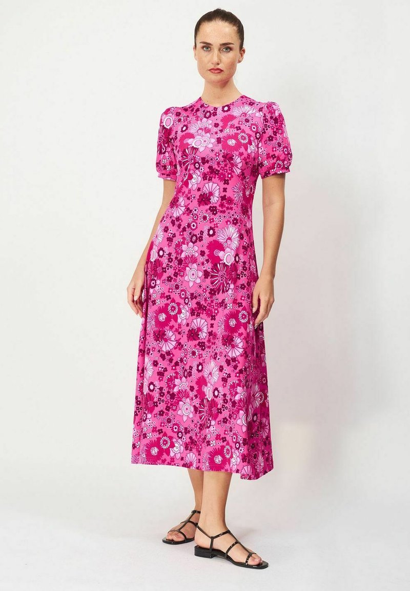 Valkoinen kukallinen maksimekko puffihihnoilla, jossa on monimuotoinen kukkakuosi ja muotoiltu vyötärö. Yhdistetty mustien nauhakenkien kanssa.