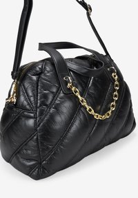 Bolso de mano de cuero negro acolchado con asas dobles, detalle con cadena dorada y cierre de cremallera. Presenta una superficie texturizada y una forma curvada.
