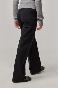 Schwarze, ausgestellte Hosen aus weicher Baumwolle, mit einer glatten Textur und feinen Nähten. Schwarze Schuhe ergänzen das Outfit.