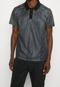 Černé polo tričko s texturovaným geometrickým vzorem, kontrastním límcem a knoflíkovou placket se třemi knoflíky. Vyrobeno ze hladkého materiálu.