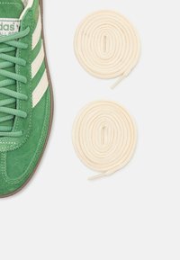 Gröna mockaskor med vita läderränder, prydda med rundade beige snören. Gummisula med mönstring och sydda detaljer.