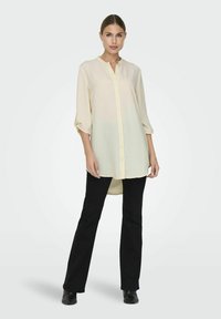 Light yellow button-up shirt with 3/4 sleeves, lightweight fabric, curved hem, paired with black pants and shoes.