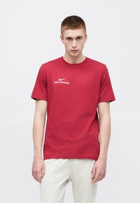 Červené bavlnené tričko s okrúhlym výstrihom, krátkymi rukávmi a bielym logom Nike s textom "NIKE OFFICIAL" na hrudi. Minimalistický dizajn.