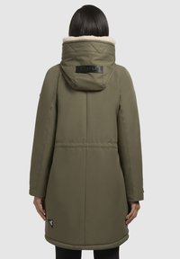 Olijfgroen lange jas met een capuchon, voorzien van een zachte voering en een cirkelvormige logo-insigne aan de onderkant. Glad materiaal met horizontale naden.