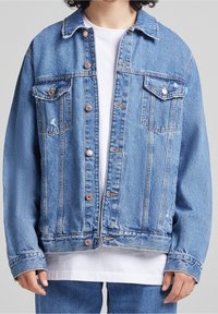 Denim jacket in light blue, featuring a button-up front, two chest pockets, and a relaxed fit. Notable fraying on collar and cuffs.