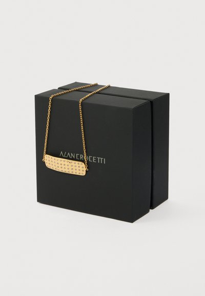 Collar de cadena de oro con un colgante rectangular incrustado con pequeños cristales, colocado sobre una caja negra con el texto de la marca.