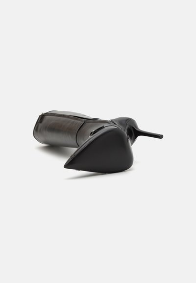 Bota de tacón stiletto de cuero negro con punta afilada y diseño aerodinámico. Presenta un acabado suave y un tacón angular. Acento de cremallera en el lado.