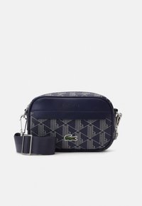 Marinblå Lacoste axelväska med geometriskt mönster, broderad krokodillogo, justerbar axelrem och silverdetaljer.