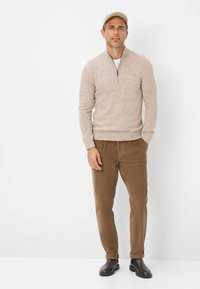 Beige Zip-Hals Pullover mit melierter Textur, kombiniert mit braunen Cordhosen und dunklen Stiefeln. Schlichtes Design, ohne sichtbare Muster.