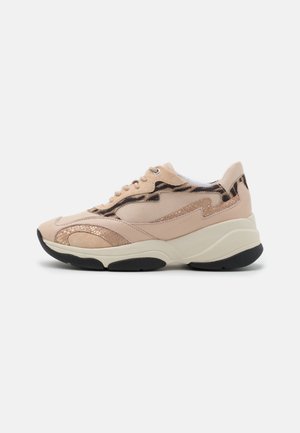 Zapatilla deportiva beige gruesa con detalles metálicos texturizados y estampado animal, suela de goma negra y cierre de cordones en la parte delantera, mostrada de lado.