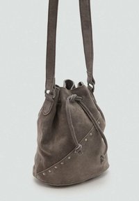 Sac seau en suede gris avec fermeture à cordon, sangles ajustables et clous décoratifs le long d'un côté, offrant une texture douce.