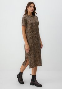 Leopardmuster-Kleid mit kurzen Ärmeln, knielang geschnitten, mit seitlichen Schlitzen, aus weichem Stoff; kombiniert mit schwarzen Knöchelstiefeln.