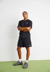 Black cotton t-shirt and shorts set with a small white logo on the chest; paired with gray athletic shoes and white ankle socks.