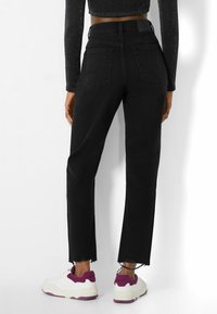 Svarta denimjeans med rak passform, fransad nederkant och två bakfickor, i kombination med vita sneakers med lila accenter.