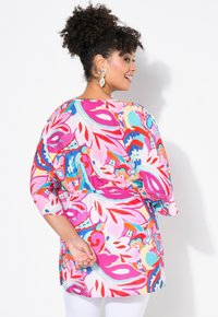 Blusa floreale colorata con un vivace motivo nei toni del rosa, rosso e blu, con vestibilità ampia e maniche a tre quarti, vita elastica.