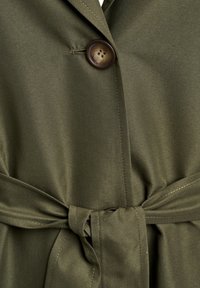 Olijfgroene jas gemaakt van gladde stof met een ronde bruine knoop, een gestrikte taille riem en op maat gemaakte revers.