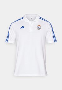 Polo blanc avec des bandes Adidas bleues sur les épaules, logo Adidas sur la poitrine droite et blason du Real Madrid sur la poitrine gauche.