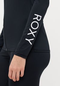 Maglietta da surf nera attillata a maniche lunghe realizzata in materiale elasticizzato con chiusura a zip; logo "ROXY" stampato in bianco sulla manica destra.