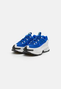 Blaue sportliche Sneaker mit einem Textil-Obermaterial, weißer und strukturierter Zwischensohle, schwarzer Gummisohle und kontrastierenden gelben Akzenten am Etikett.