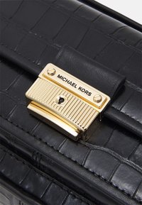 Borsa a mano in pelle nera con motivo a coccodrillo testurizzato, dotata di una chiusura in metallo dorato incisa con "MICHAEL KORS".