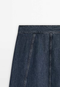 Tumman denim-hameen vyötärö on istuva, ja siinä on laskoksia sekä näkyviä ompeleita. Kangas on sileä ja väriltään tasainen.