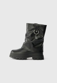 Botas negras plegables de cuero sintético, con suela gruesa, correa con un acento en forma de anillo y superficie texturizada.