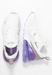 Zapatillas de malla blancas con acentos morados, que presentan un gran talón de burbuja de aire transparente morado, parte superior texturizada y cierre de cordones sencillo.