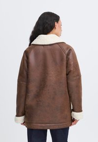 Giubbotto in similpelle marrone con colletto e polsini in pile bianco, caratterizzato da una vestibilità rilassata e dettagli di cucitura a vista.