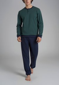 Felpa verde a fantasia con polsini blu navy, dotata di scollo rotondo e patta con tre bottoni, abbinata a pantaloni blu navy. Tessuto morbido.